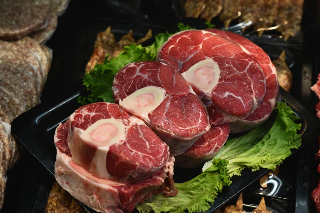 Close-up of fresh raw osso buco on display with green lettuce leaves.