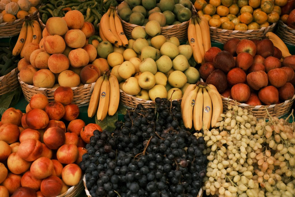 Colorful display of assorted fruits including apples, bananas, grapes, and peaches at an outdoor market.